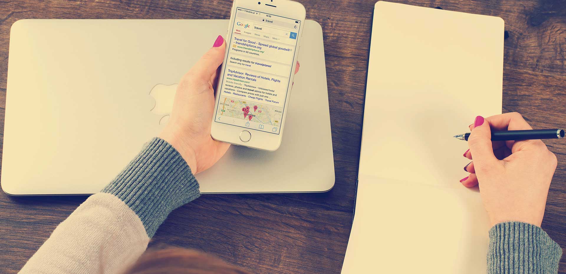 Image showing closed laptop with womans hands holding i-phone beside open notebook holding pen poised to write notes.