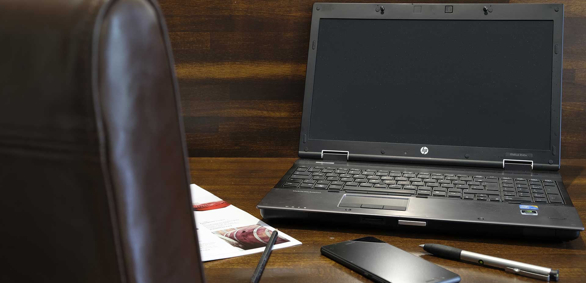 Image with back of leather executive chair and open laptop on desk with pen, pencil, phone and brochure on desk